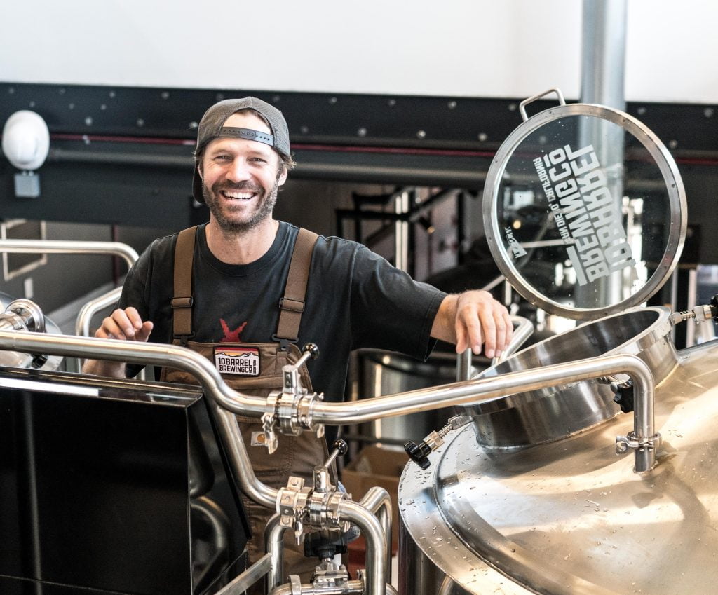 Man smiling with cap on backwards near beer pumps