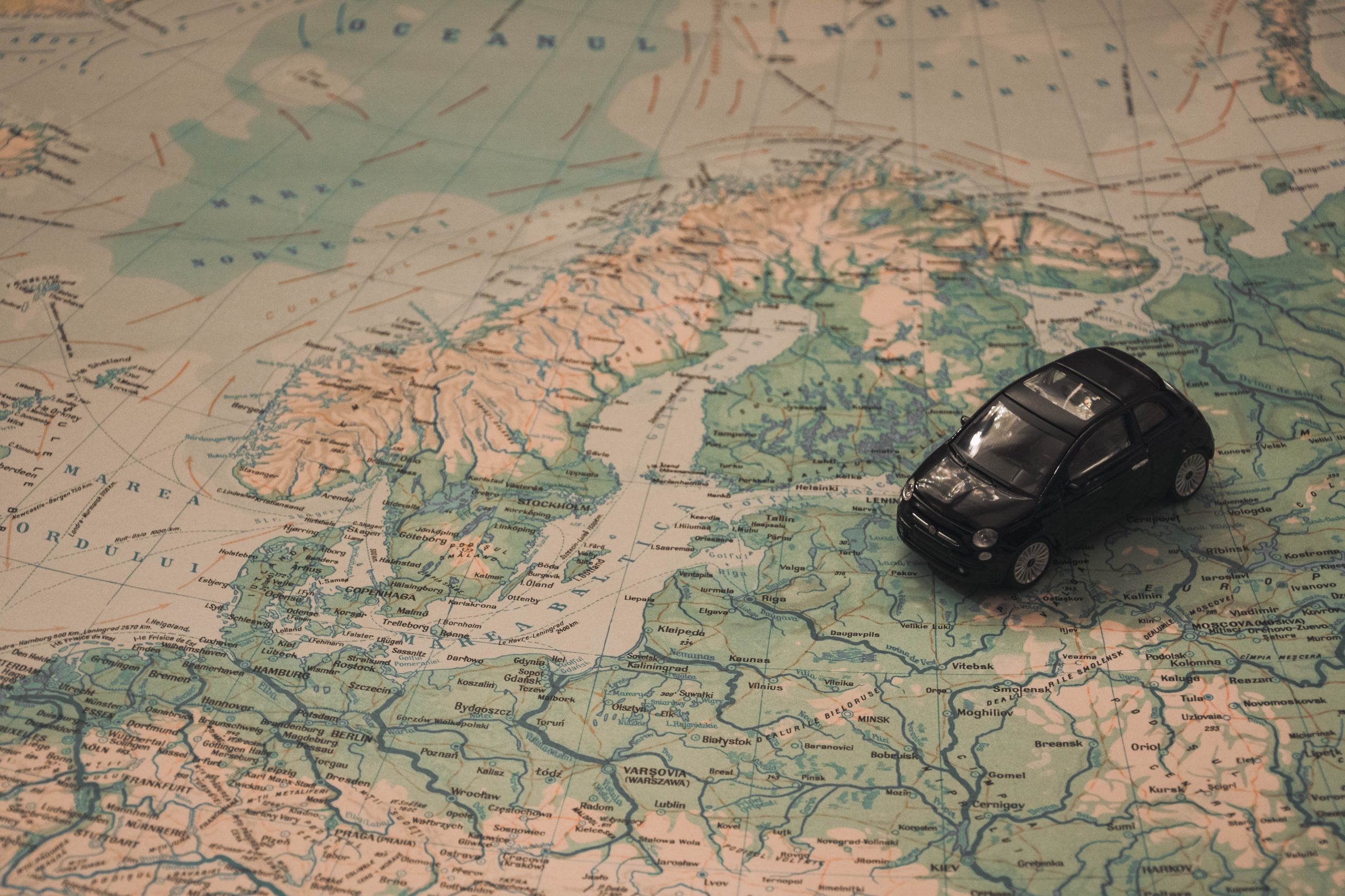 little black car travelling across a printed map of Europe
